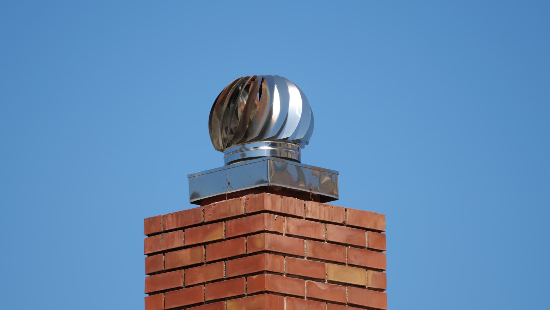 Sanierter Klinkerschornstein mit Edelstahl-Aufsatz und Turbulator gegen blauen Himmel